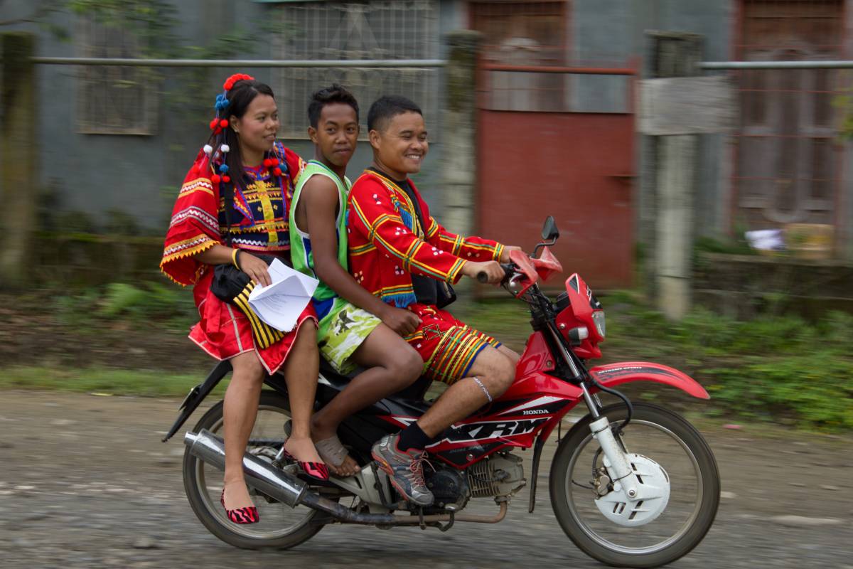 Three people riding a motorcycle with traditional attire on in the Philippines.